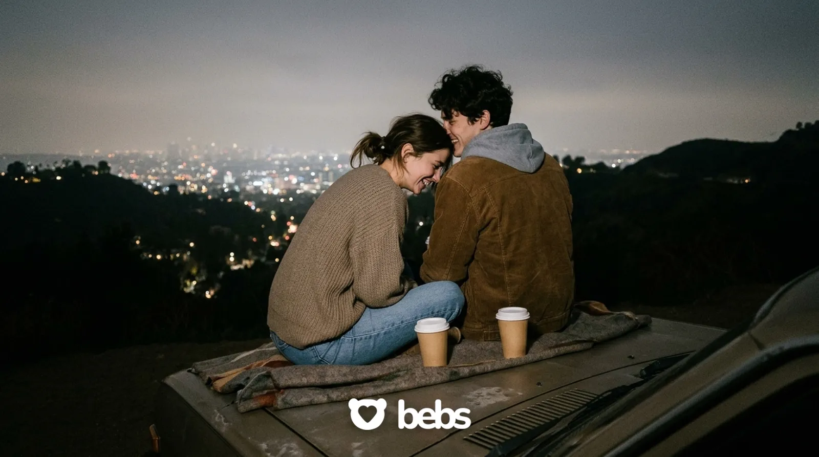 Couple sitting on a car hood with coffee above the city lights on Mulholland Drive, cozy date night ideas in Los Angeles