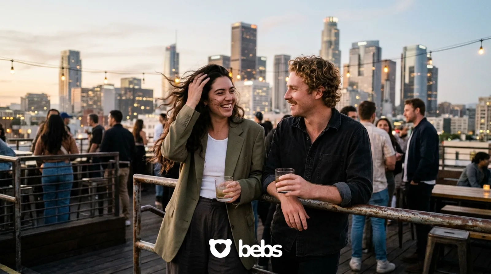 Couple laughing at a downtown rooftop bar at dusk with the city skyline behind, rooftop date night ideas in Los Angeles